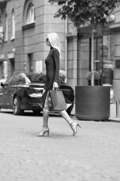 photo of pretty woman crossing the street with shopper bags. woman with shopper bags outdoor. woman with shopper bags in the street. woman with shopper bags outside.