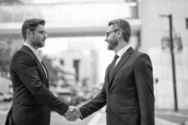 İki neşeli iş ortağı el sıkışma ile ilgileniyor. İki iş ortağı dışarıda iş yapıyor. İki iş ortağının dağıtırken çekilmiş fotoğrafı. iki iş ortağı.