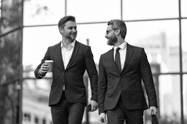 Gülümseyen takım elbiseli iş ortakları kahve molasında pazarlık ediyorlar. İş ortaklarının resmi ara verildiğinde görüşür. İş ortakları ara verildiğinde sokakta pazarlık yaparlar. İş ortakları ara verildiğinde görüşür