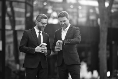 İşletme yöneticisi kontrol saati sokakta. İşletme yöneticisi dışarıda kontrol zamanı. Takım elbiseli bir işletme yöneticisi kahve tutuyor. İş yürütme denetim zamanının fotoğrafı.