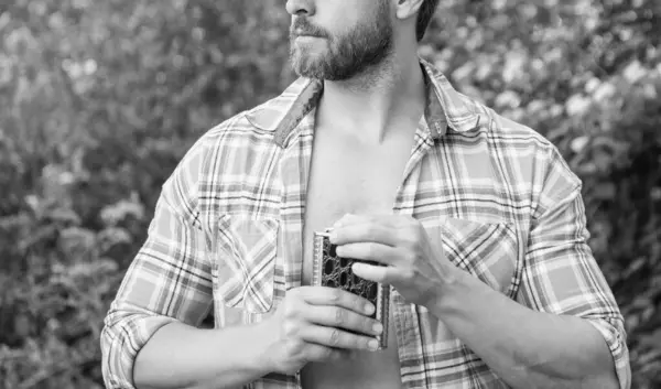 cropped view of man with whiskey flask. man with whiskey flask outdoor. man with whiskey flask wear checkered shirt. photo of man with whiskey flask.