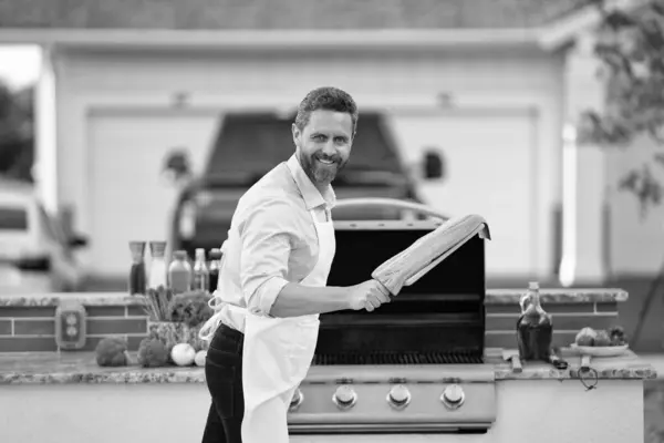 stock image photo of glad man barbecuing trout fillet on grill. man barbecuing trout fillet. man barbecuing trout fillet outdoor. man barbecuing trout fillet at backyard.