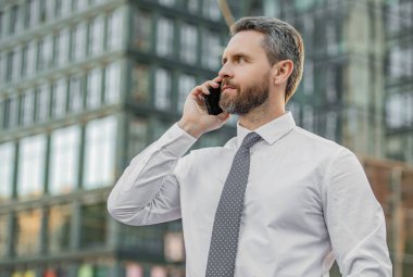 handsome businessman having smartphone call in the street. businessman call on smartphone outside. photo of businessman call on smartphone and talk. businessman has smartphone call outdoor.