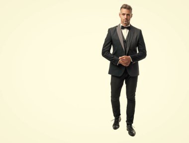 Zengin smokin papyonlu hırslı damat beyaz arka planda izole edilmiş. Tam uzunluk.