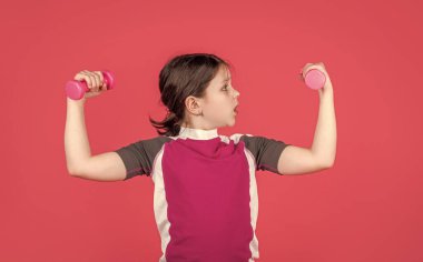 Şok olmuş çocuk pembe arka planda fitness halterleri tutuyor..