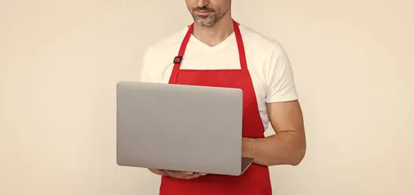 mature man in apron chatting on computer.