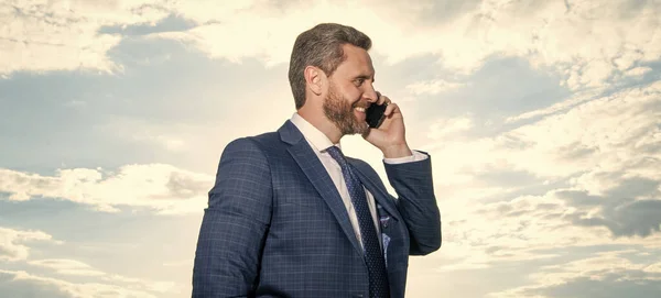 cheerful man has phone talk on sky background. man has phone talk outdoor. man has phone talk wear suit. photo of man has phone talk.