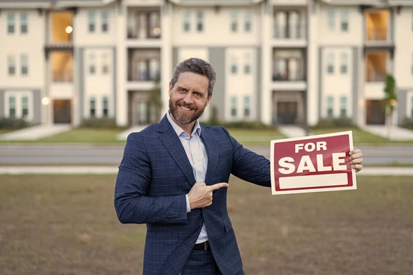 photo of broker with for sale board, point finger. sale property by broker. man broker hold board for sale property. sale property by broker outdoor.