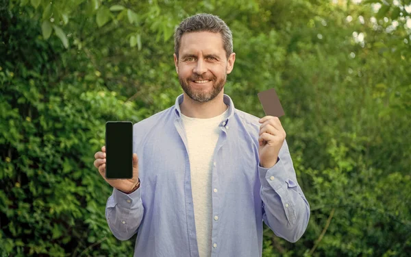 glad man presenting smartphone outdoor. man presenting smartphone screen with copy space. photo of man presenting smartphone. man presenting smartphone.