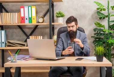 Kendine güvenen sakallı patron internette bilgisayarla çalışıyor. Ofiste kahve var, modern hayat..