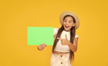 Sarı arka planda yeşil kağıtta fotokopi alanı olan mutlu genç kız. işaret parmağı.