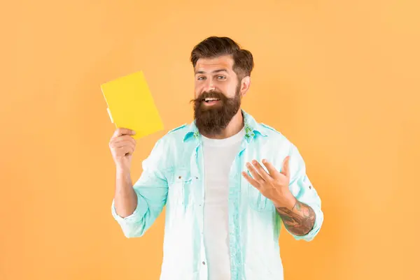 happy bearded man presenting book on yellow background, advertisement.