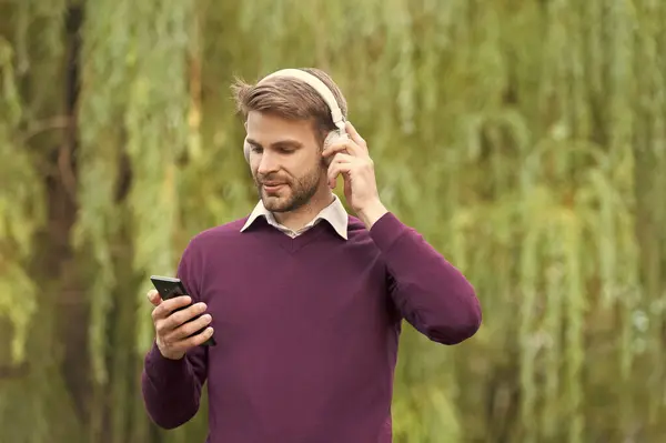 young handsome man listen music in headphones and chating on smartphone outdoor.