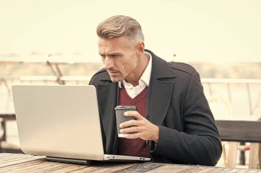 Ciddi bir patron laptopta çalışıyor açık kafede kahve içiyor..