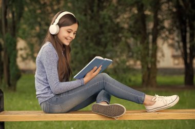 Sesli kitap konsepti. Okul çıkışı kulaklıkla okuyup dinleyen mutlu genç kız, sesli kitap..