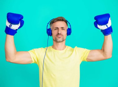 Spor salonundaki sporcu. Spor giyim bölümünde boksör. Egzersiz ve yumruk. Mavi eldivenli sporcu. Kulaklık takan olgun bir boksör. Sporcu boks. Güçlü adam müzik dinler. Güç gösteriliyor.