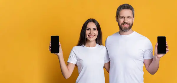 Advertisement presentation copy space. Couple presenting phone screen. Couple showing smartphone isolated on yellow. Man and woman showing phone app. Family blog. Product proposal. Copy space.