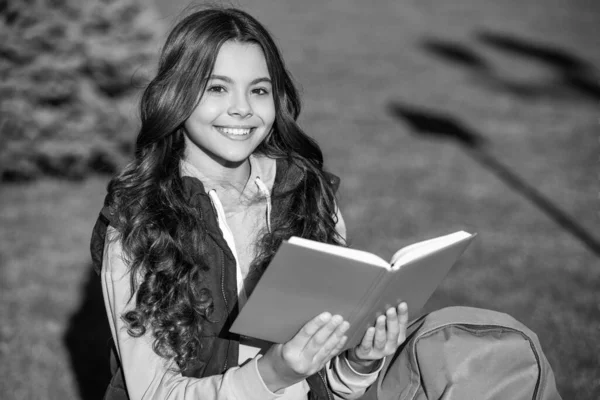 glad school teen girl read outdoor. school teen girl read outside. school teen girl read book. photo of school teen girl read in park.