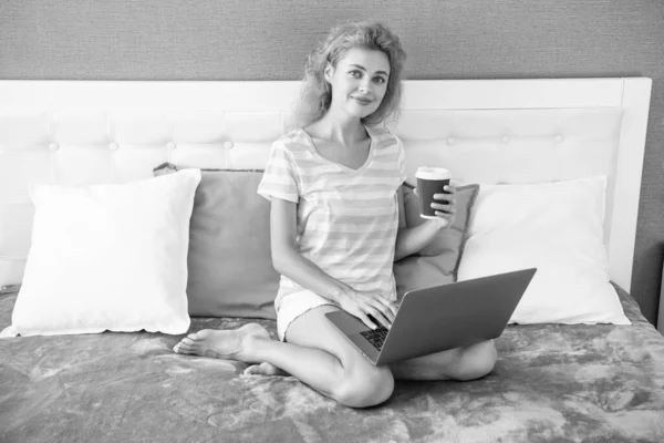 woman freelancer holding coffee blogging on laptop. freelancer woman blogging at home. home blogging for freelancer. woman in bed with laptop.