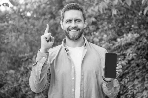 photo of inspired man presenting smartphone. man presenting smartphone. man presenting smartphone outdoor. man presenting smartphone screen with copy space.