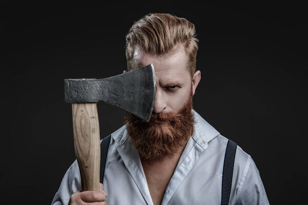 Brutal man in suspenders with ax isolated on black. Mature redhead man with hairstyle. Brutal male fashion style. Male brutality. Vintage brutality guy with ax in retro suspenders. Barbershop concept.
