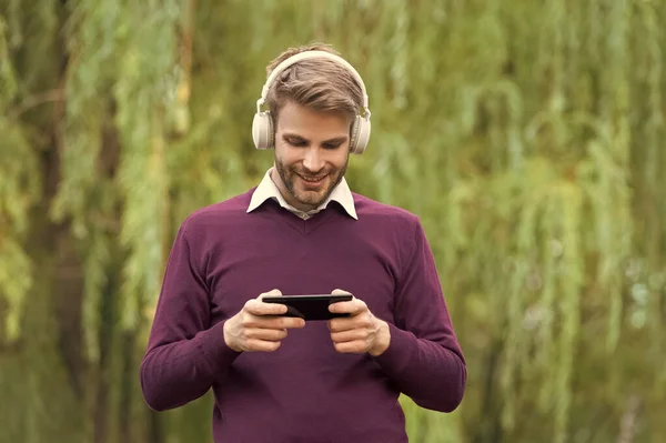 young handsome man listen music in headphones and do internet surfing on phone outdoor.