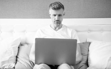 mature freelancer working on laptop in bed.