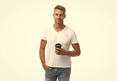 Beyaz üzerine izole edilmiş kahveyle gülümseyen mutlu adam. Paket kâğıt bardakta kahve tutan adam. Kahve içen, stüdyosu olan beyaz tişörtlü yakışıklı bir adam..