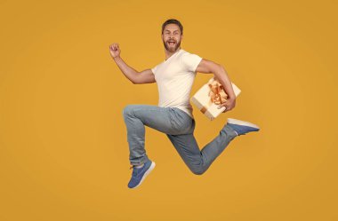 Havadaki sarı stüdyo arka planında bir hediye kuryesi. Enerjik adam hediye kutusuyla hızlı koşuyor. Hediye ve hediye teslimi.