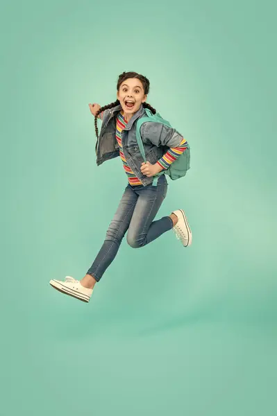 Energetic teenager screaming in midair, school. Excited girl jumping after school blue background. Back to school.
