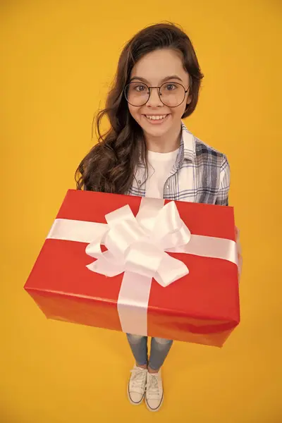 glad teen child with present isolated on yellow background. teen child in glasses with present. studio shot of teen child hold present. teen child holding box of present.