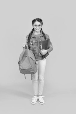 Happy teenage girl holding school bag yellow background. School education. Back to school.