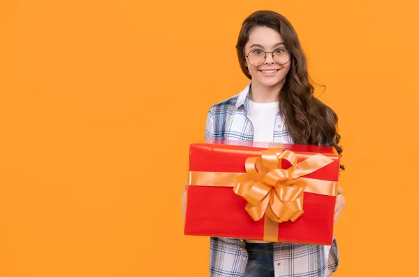 teen girl with present isolated on yellow background with copy space. teen girl in glasses with present. studio shot of teen girl hold present. teen girl holding box of present.
