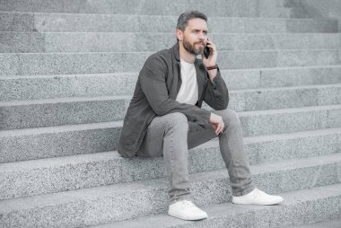 Adam akıllı telefon konuşması. Adam dışarıda otururken akıllı telefondan konuşuyor. Erkek erkeğe konuşmanın akıllı telefon iletişimi. Yetişkin adam akıllı telefonda konuşur..