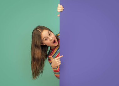 Reklam için fotokopi alanı olan boş mavi kağıdın arkasında sürpriz bir çocuk. işaret parmağı.