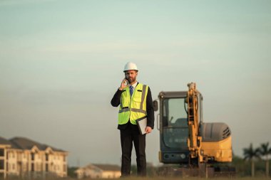 Mimar işgali adamı telefonda konuşuyor. Mimarların adamı açık havada çalışıyor. Mimar işgali mühendisi kask takıyor. Mimarlık mesleğinin fotoğrafı..