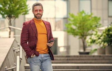 Akıllı telefondan ceketle mesajlaşan adamın fotoğrafı, kopyalama alanı. Adam dışarıda akıllı telefondan mesaj atıyor. Adam sokakta akıllı telefondan mesaj atıyor. Adam dışarıda akıllı telefondan mesaj atıyor..