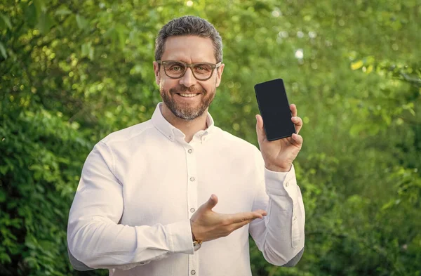 smiling businessman showing app. businessman showing app outdoor. businessman showing app on phone. photo of businessman showing app with copy space.