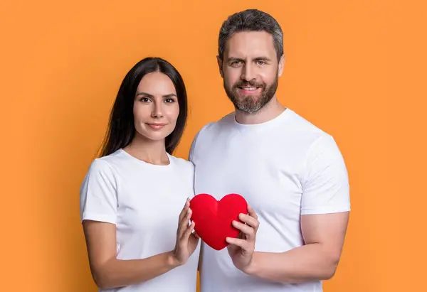 couple in love with valentine heart isolated on yellow. couple with valentine love heart in studio. valentine holiday love couple with red heart. photo of couple in love with valentine heart.