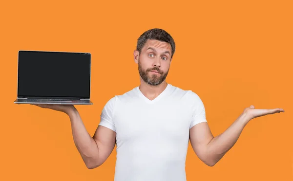 puzzled man showing portable laptop isolated on yellow background. man presenting portable laptop in studio. man showing portable laptop. man presenting screen of portable laptop with copy space.