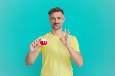 Erkek kozmetik ürünü sunan adam. Mavi renkte yüz kremi gösteren bir adam var. Olgun adam cilt kremi kullanır. Günlük alışkanlık ve kişisel bakım. Cilt güzelliği. Erkek güzellik kozmetiği. Tamam..