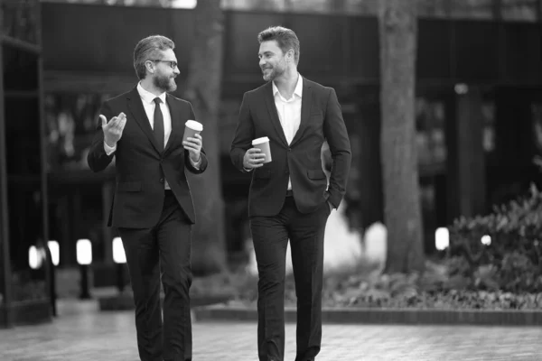 photo of executive discussing business walk with coffee. executive discussing business in the street. executive discussing business outdoor. executive in suit discussing business holding coffee.