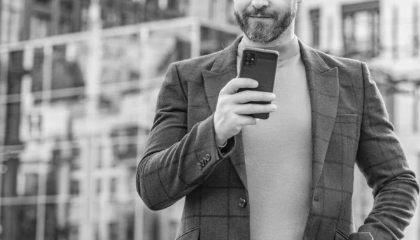 cropped view of man messaging on smartphone outside. photo of man messaging on smartphone in jacket. man messaging on smartphone outdoor. man messaging on smartphone in the street.