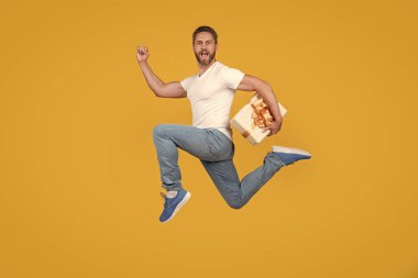 Enerjik adam hediye kutusuyla hızlı koşuyor. Havada sarı arka planda bir hediye kuryesi. Hediye ve hediye teslimi.