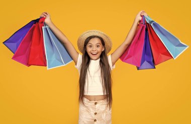 Sarı arka planda alışveriş torbaları olan hayret verici bir genç kız..