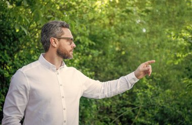 Gözlüklü yakışıklı profesyonel adam parmak göstererek doğal arka plan, kopyalama alanı.