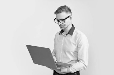 Gri arka planda bilgisayar üzerinde çalışan gözlüklü olgun işveren.