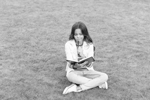 Not defterine not alan genç kız çimlere oturuyor. Not alıyorum. Öğrenci dışarıda notlar alıyor..