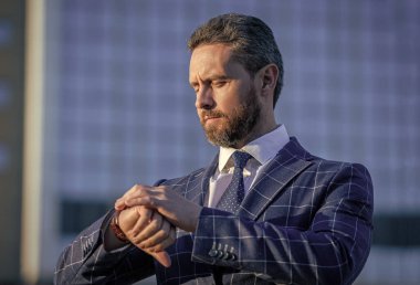 Ceket ve saat giymiş dakik bir iş adamı. Dakik iş adamı dışarıda duruyor. Formalite icabı dakik bir iş adamı. Dakik iş adamı dışarıyı gözetleme süresini kontrol et.