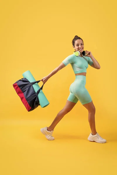 positive fitness woman in sportswear walk with sport bag in studio. fitness woman in workout sportswear isolated on yellow background. fitness and sportswear.